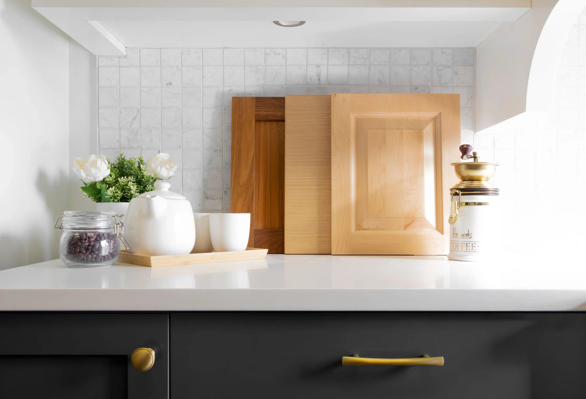 Two unfinished wood cabinet doors propped against a tiled backsplash on a kitchen counter